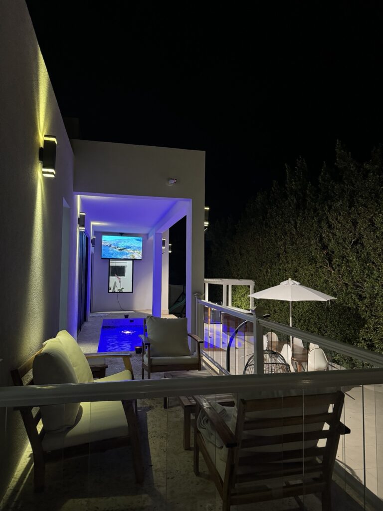 Covered guest house terrace with seating and pool view at night